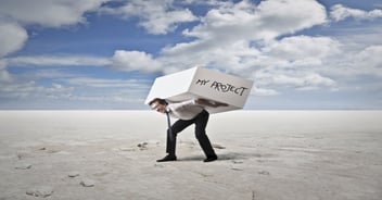 Business professional struggling to carry a large box labeled “My Project,” symbolizing the challenges, complexity, and workload involved in an Acumatica ERP implementation.