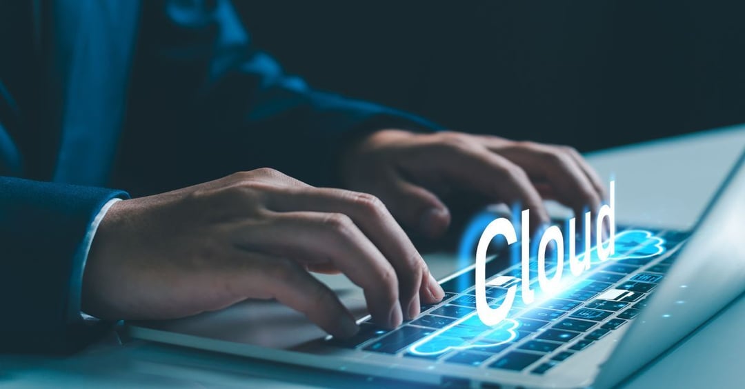Close-up of a professional typing on a laptop keyboard with a glowing “Cloud” interface overlay, symbolizing cloud computing, SaaS platforms, and enterprise cloud technology adoption.