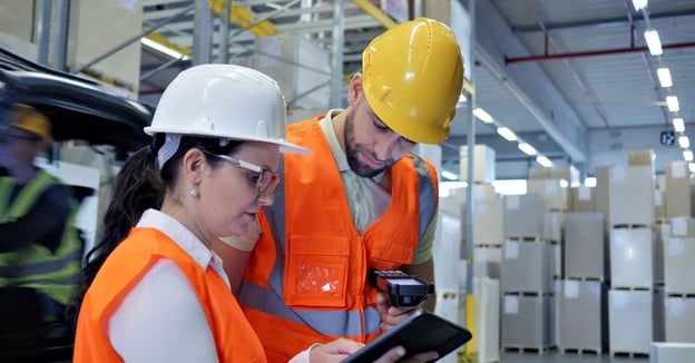 Warehouse workers using tablet and barcode scanner to manage inventory in a modern distribution center.