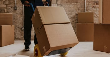Worker moving stacked boxes on a hand truck, illustrating the risks of a Lift and Shift ERP Migration.
