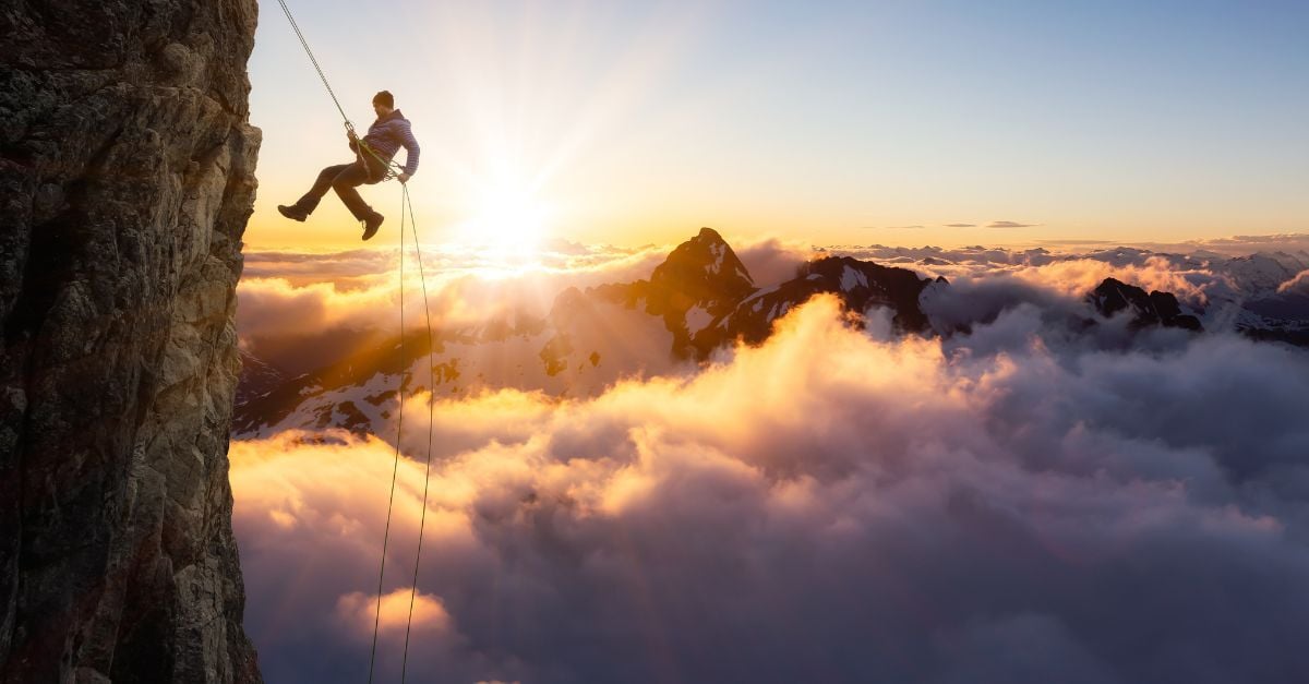 Climber rappelling off a cliff above clouds at sunrise, symbolizing Cloud ERP risks and high-stakes decisions