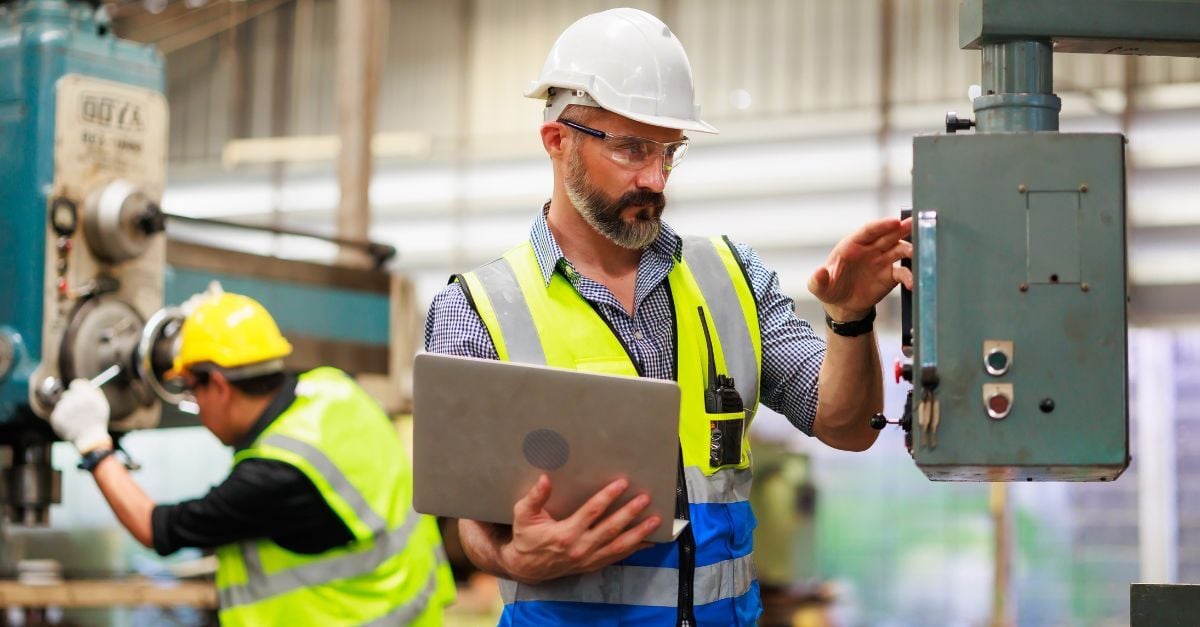 Epicor to SAP Business One migration engineer inspecting industrial machine with laptop on factory floor