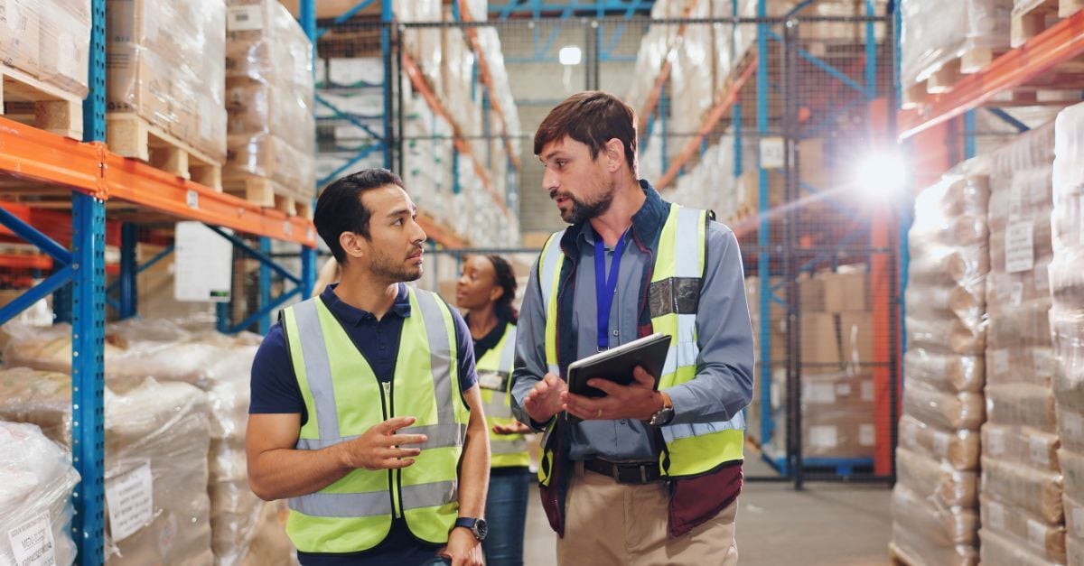Two warehouse workers discuss operations while reviewing a tablet, highlighting the long-term cost of ERP mistakes.