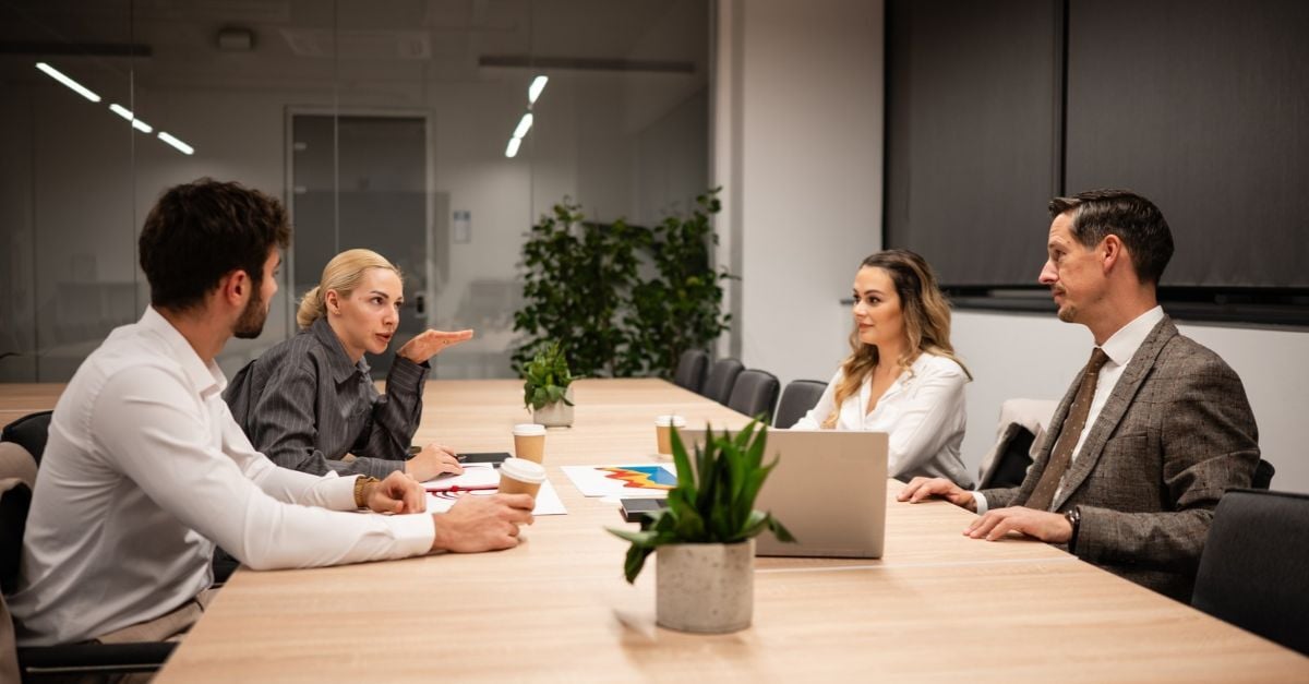 Four business professionals discuss ERP architecture around a conference table with a laptop and documents.